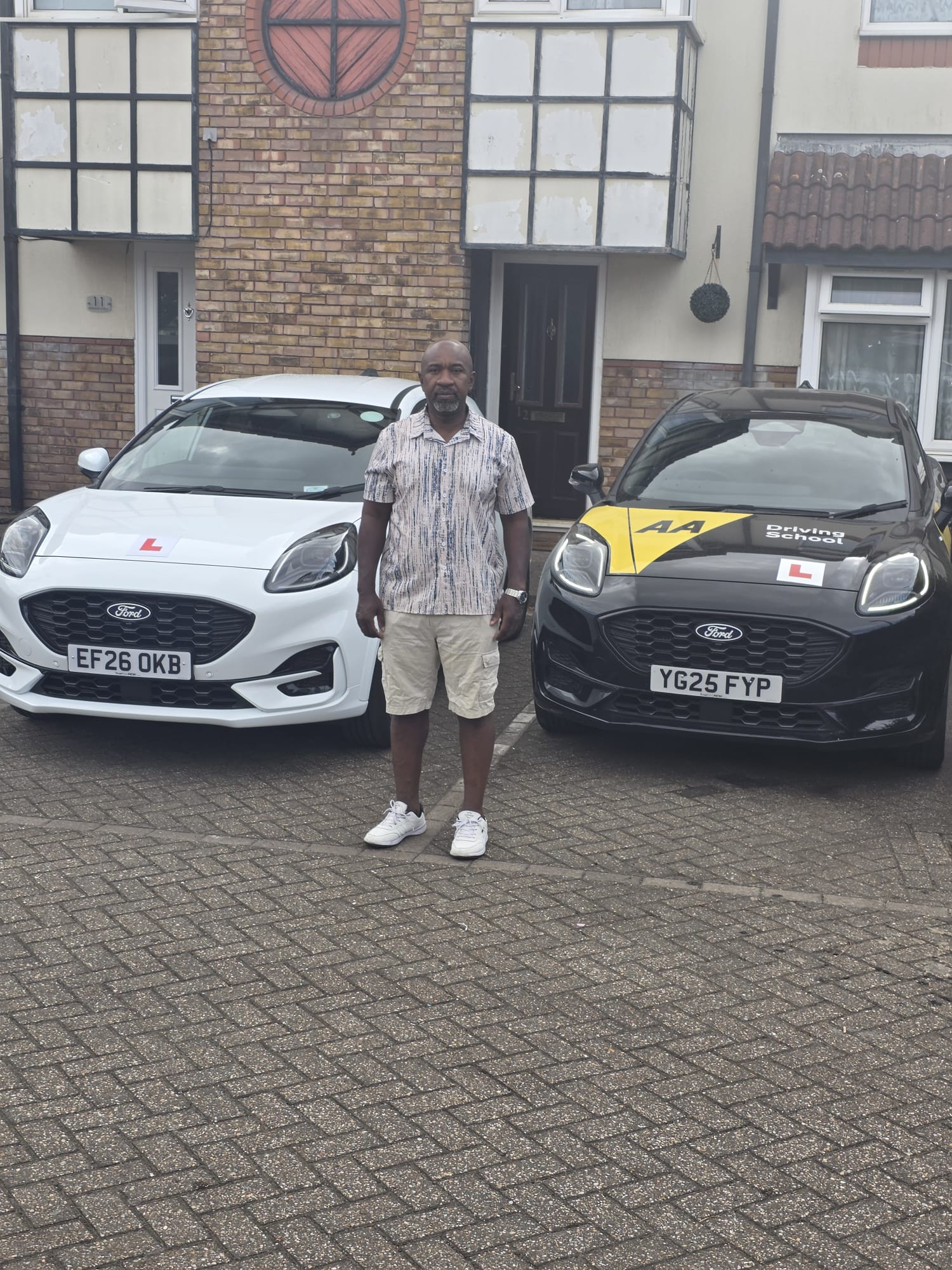 Charles standing between his two dual-control Ford Puma driving school cars